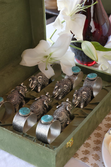 Silver elephant napkin rings and turquoise-set cuffs arranged in an open olive velvet box with white lilies