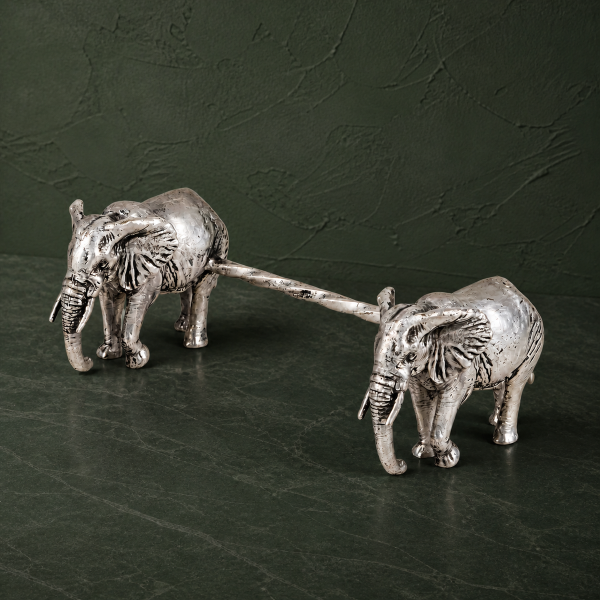 Two silver-plated elephant spoon rests on a dark green studio surface