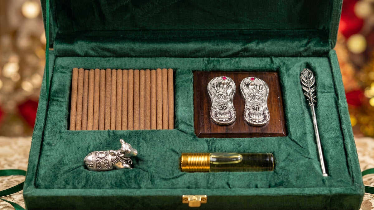 Pooja Ghar gift box open, holding incense sticks, a silver-plated Vishnu Paduka on a wooden base, a Nandi dhoop stand, a peacock feather tilak stick and a roll-on oudh attar