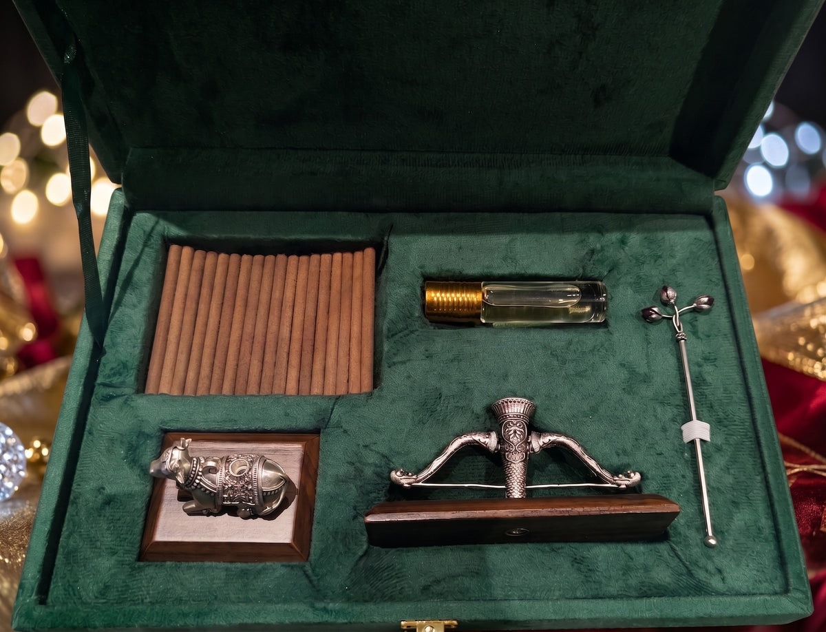 Sugandh pooja gift box open, holding oudh incense sticks, a roll-on oudh attar, a Nandi dhoop stand on a wooden base, a Ram Dhanush agarbatti stand and a lotus bud tilak stick, all in pure silver plating