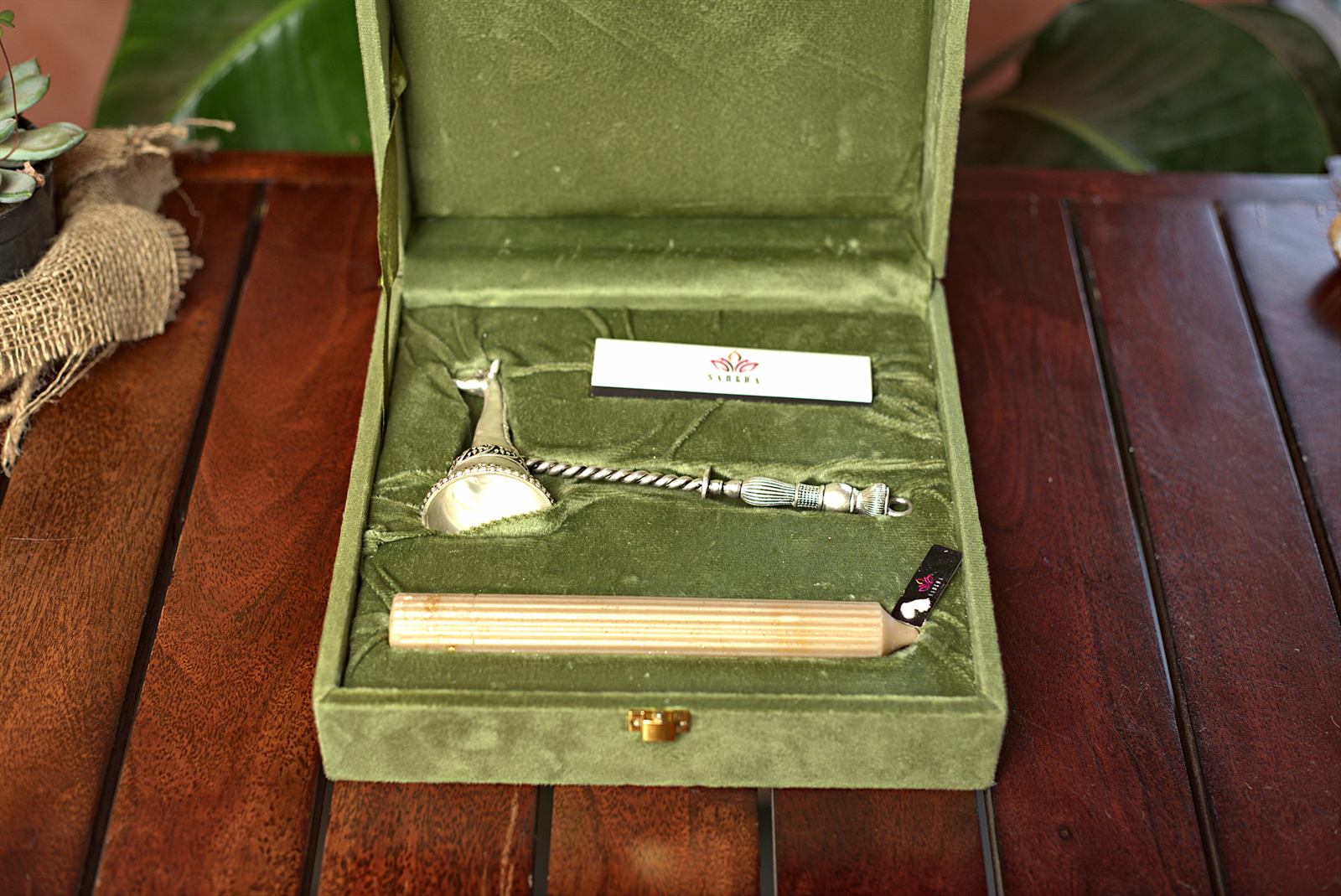 Silver-toned candle snuffer and candle presented in an open sage velvet SABERA gift box.