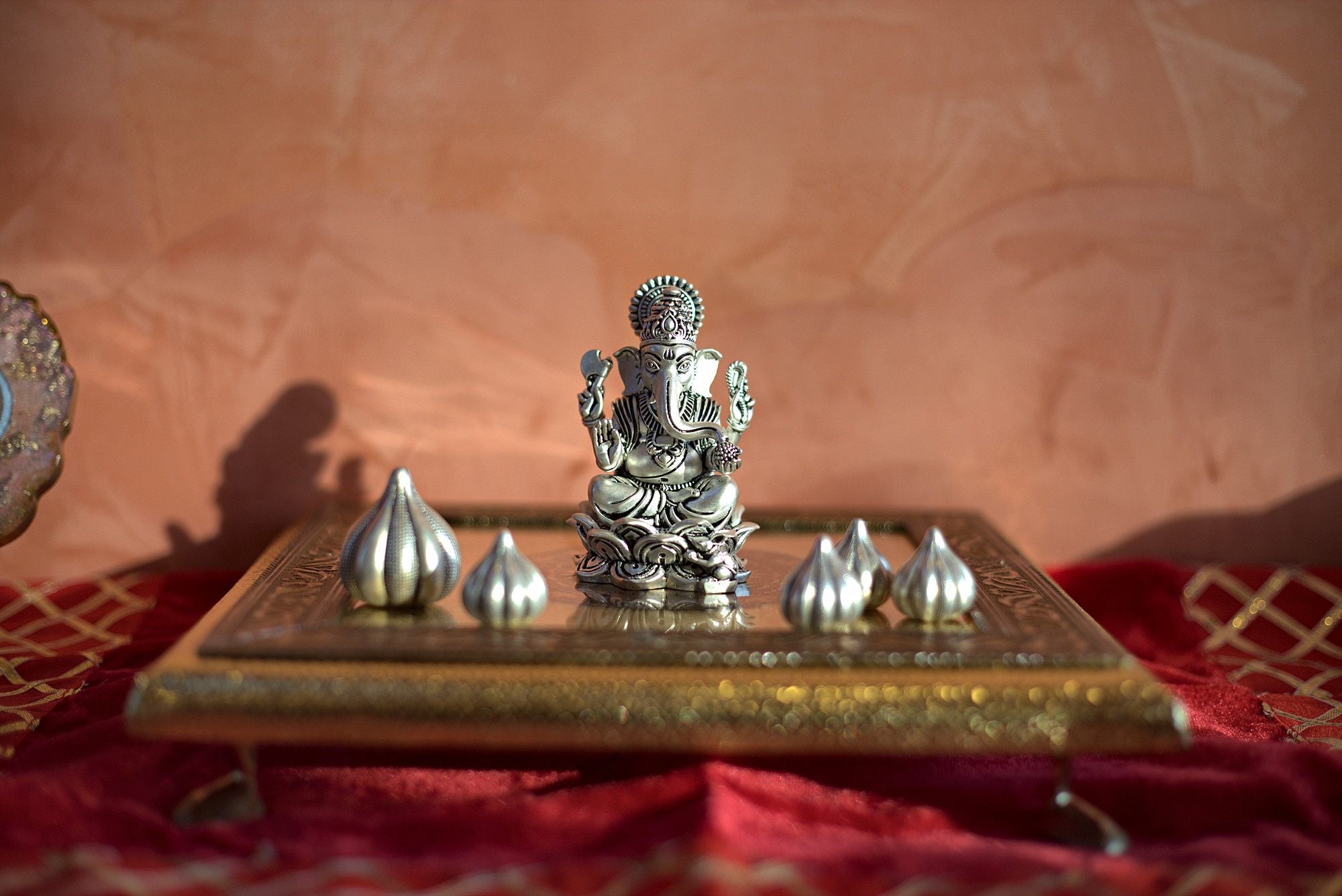 Silver-toned Ganapati idol arranged with decorative modaks on a ceremonial tray.