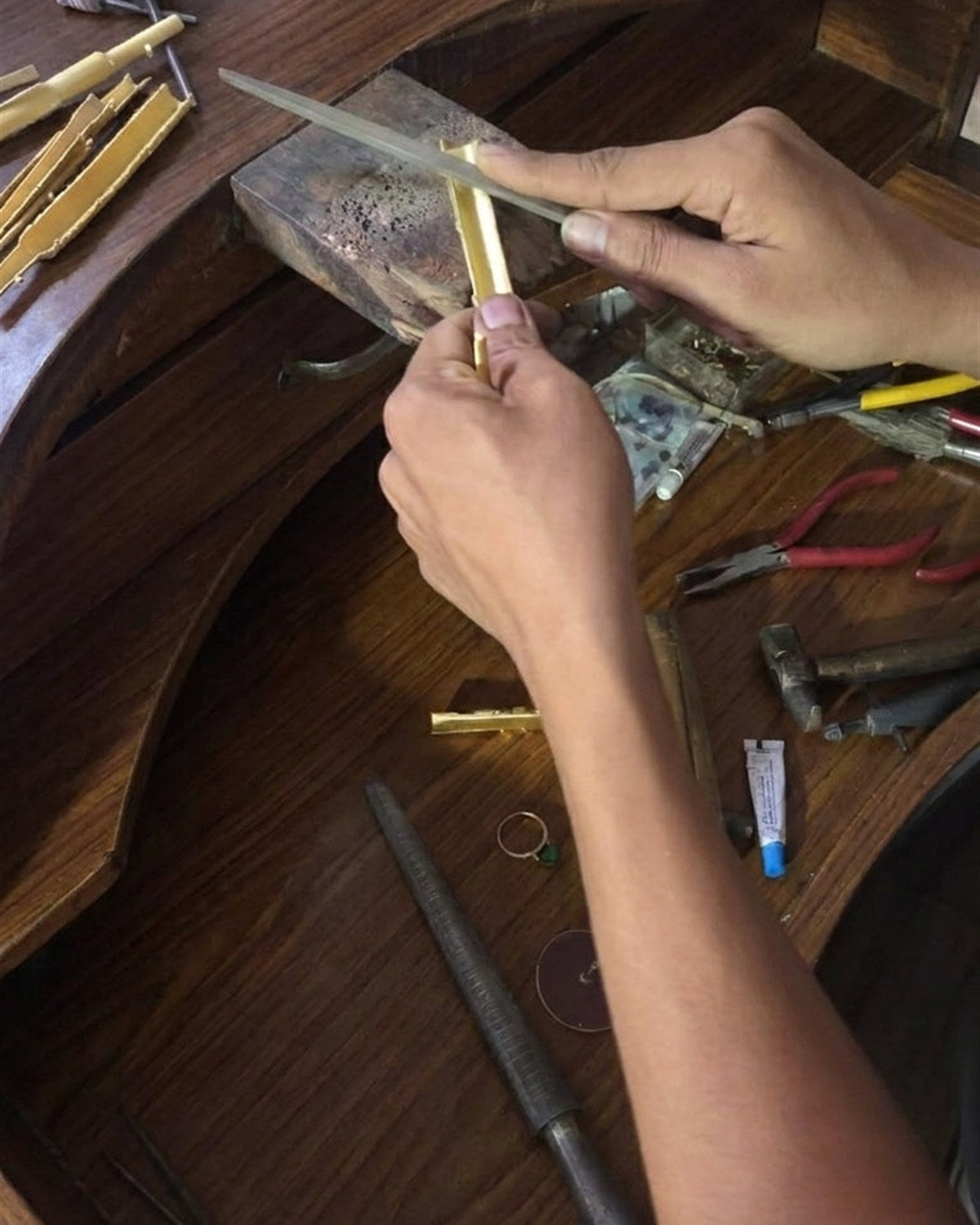 Karigar filing a brass hookah tip by hand at a Jaipur workbench.